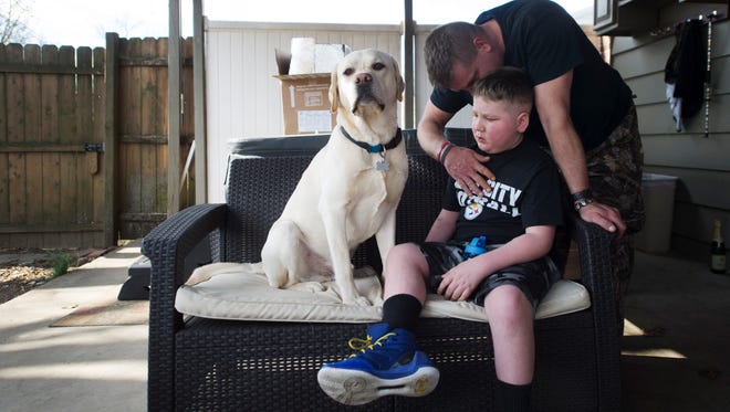 Bill Kohler comforts his son, Ayden Ziegler-Kohler, 10, as he sits on their patio with his dog, Zuko. Ayden, who has a rare childhood cancer and limited mobility, was upset after seeing other kids out playing on the playground.