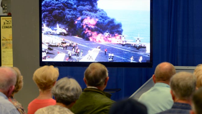 The crowd watches footage of the fire aboard the USS Forrestal in 1967 during the 50th anniversary commemoration ceremony at the National Naval Aviation Museum Saturday, July 29, 2017.