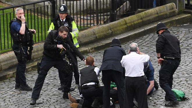 A policeman points a gun at a man on the ground as emergency services attend the scene outside the Palace of Westminster, London.