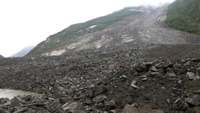 In this photo released by China's Xinhua News Agency, emergency personnel, in orange, work at the site of a landslide in Xinmo village in Maoxian County in southwestern China's Sichuan Province, Saturday, June 24, 2017. Around 100 people are feared buried by a landslide that unleashed huge rocks and a mass of earth that crashed into their homes Saturday, a county government said. (He Qinghai/Xinhua via AP) ORG XMIT: XIN802