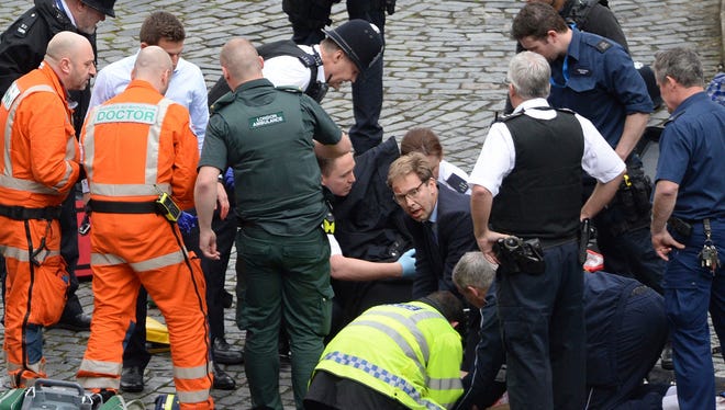 Conservative Member of Parliament Tobias Ellwood, center, helps emergency services attend to an injured person outside the Houses of Parliament in London.