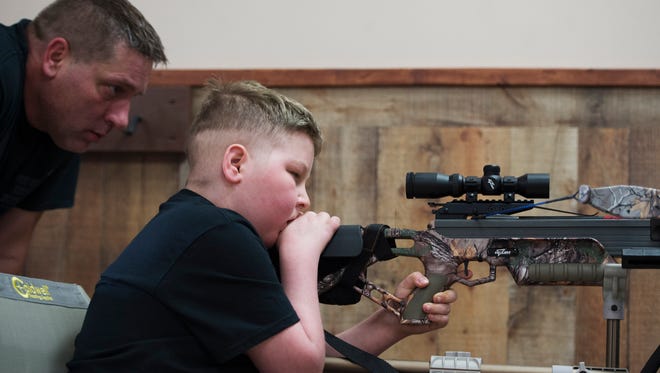 Bill Kohler watches over his son's shoulder as he shoots a target at Xtreme Archery in Springettsbury Township. Ayden was practicing for an upcoming hog and ram hunt. Though cancer has limited his mobility, a special chair with an extended arm helps stabilize the bow so Ayden can still shoot.