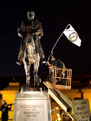 A worker in protective gear takes down an Army National Guard flag from the statue of Confederate General P.G.T. Beauregard during the statue's removal from the entrance to City Park in New Orleans, Tuesday, May 16, 2017.