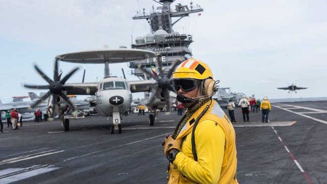 Yellow shirt aircraft handlers and directors coordinate the movement of aircraft on the USS Dwight D. Eisenhower flight deck as an E-2 Hawkeye is readied for launch while a F/A-18E Super Hornet lands.