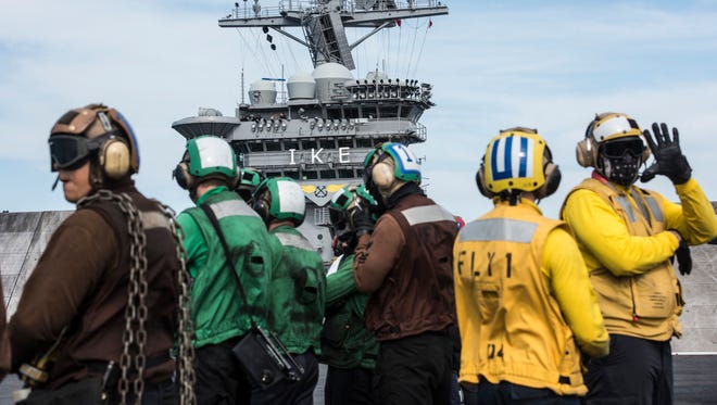 USS Eisenhower flight deck crew members during flight operations. Yellow shirts coordinate the movement of aircraft, the brown shirts are plane captains, and the green shirts are catapult crew.