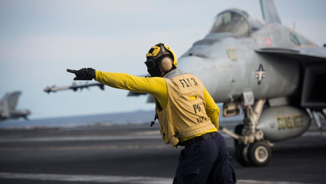 Yellow-shirt aircraft handlers and directors a F/A-18E Super Hornet on the deck of the USS Eisenhower.