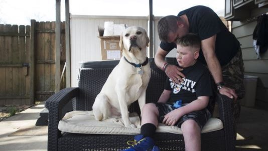 Bill Kohler comforts his son, Ayden Ziegler-Kohler, 10, as he sits on their patio with his dog, Zuko. Ayden, who has a rare childhood cancer and limited mobility, was upset after seeing other kids out playing on the playground.