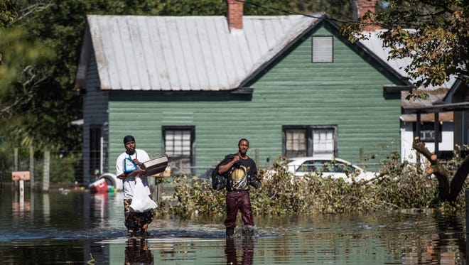 Wayne Edwards, left, and Vance Barden  carry personal items through a flooded street caused by Hurricane Matthew on Oct. 11, 2016, in Fair Bluff, N.C.